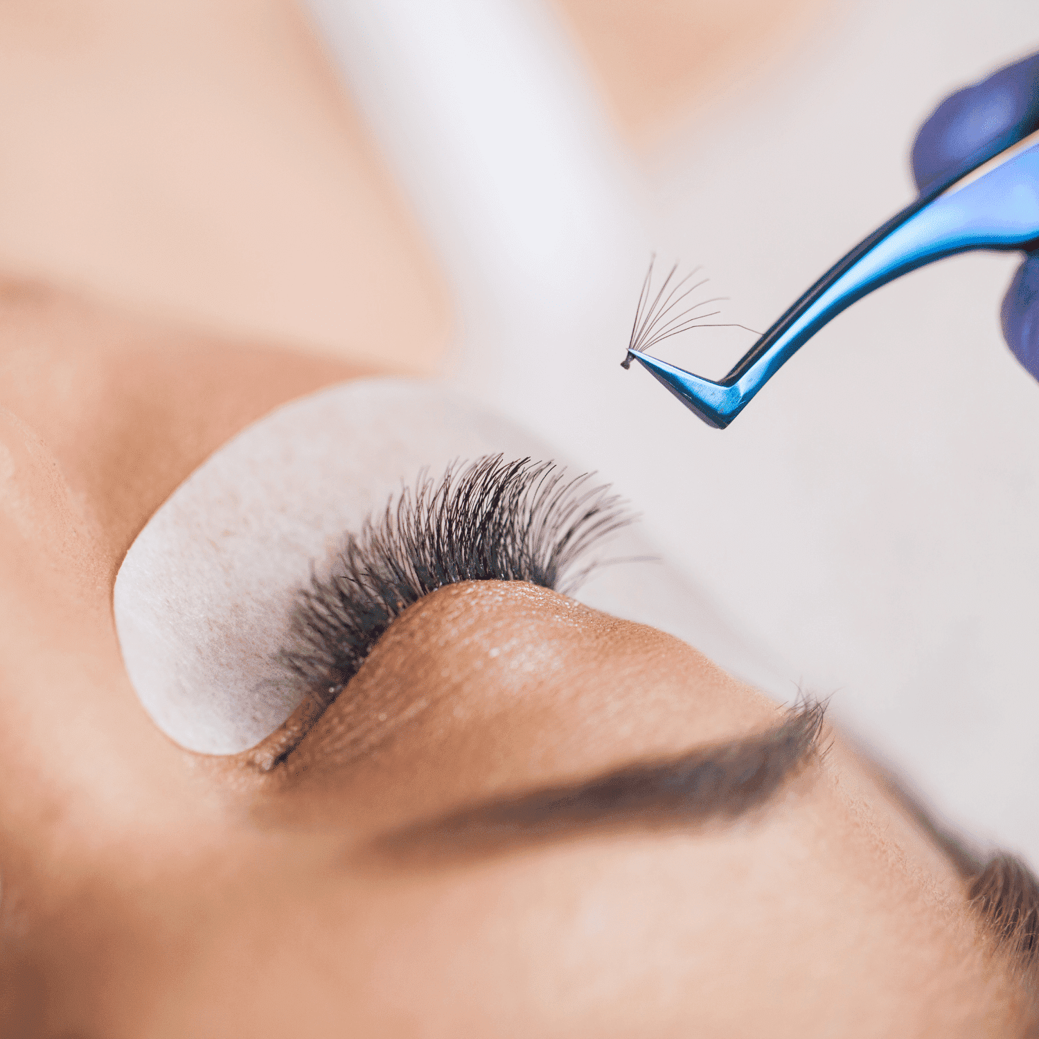 Applying eyelash extensions with tweezers on person’s eye with a protective pad.