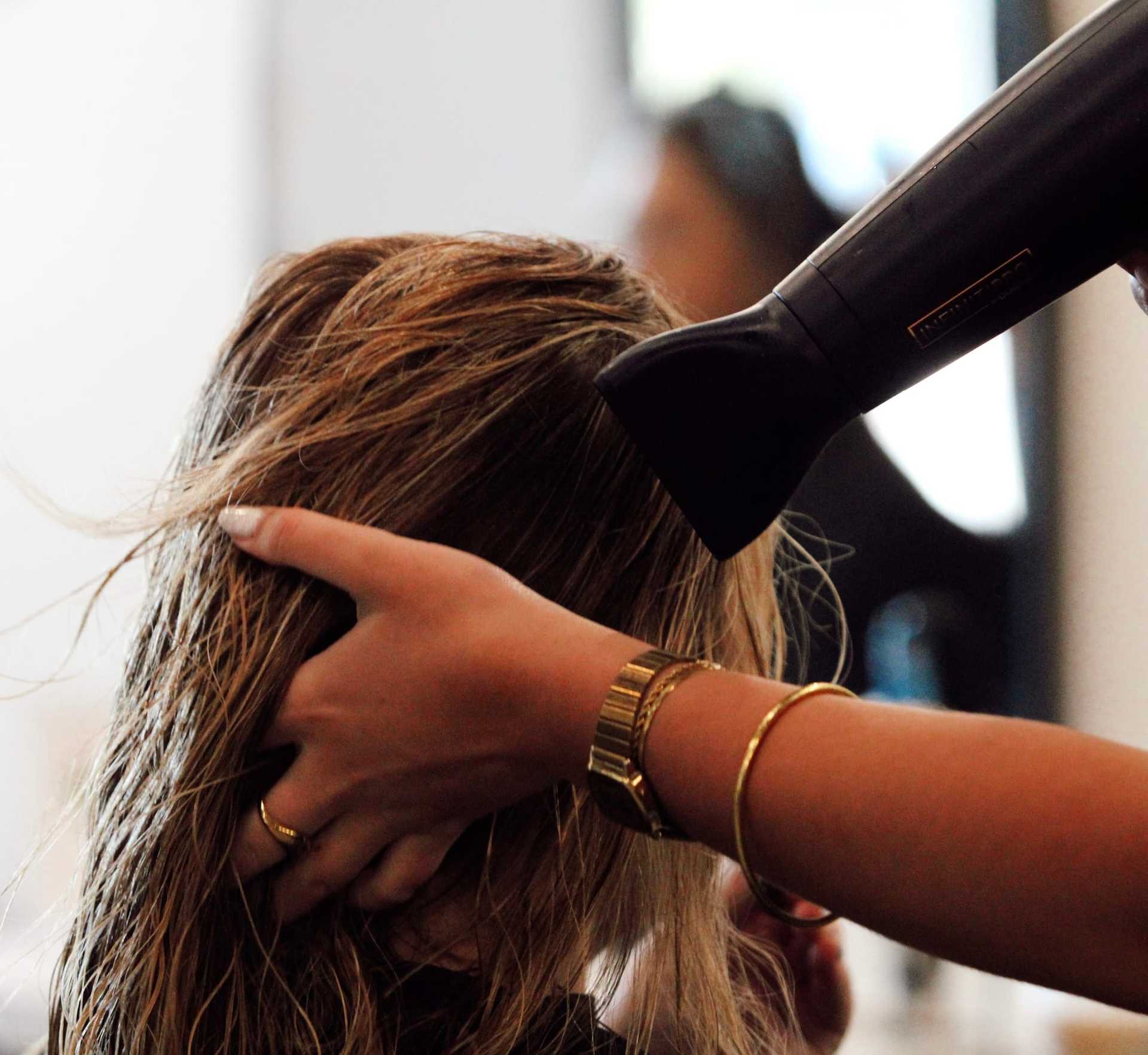 Blow-drying wet hair in a salon by a stylist with gold bracelets.