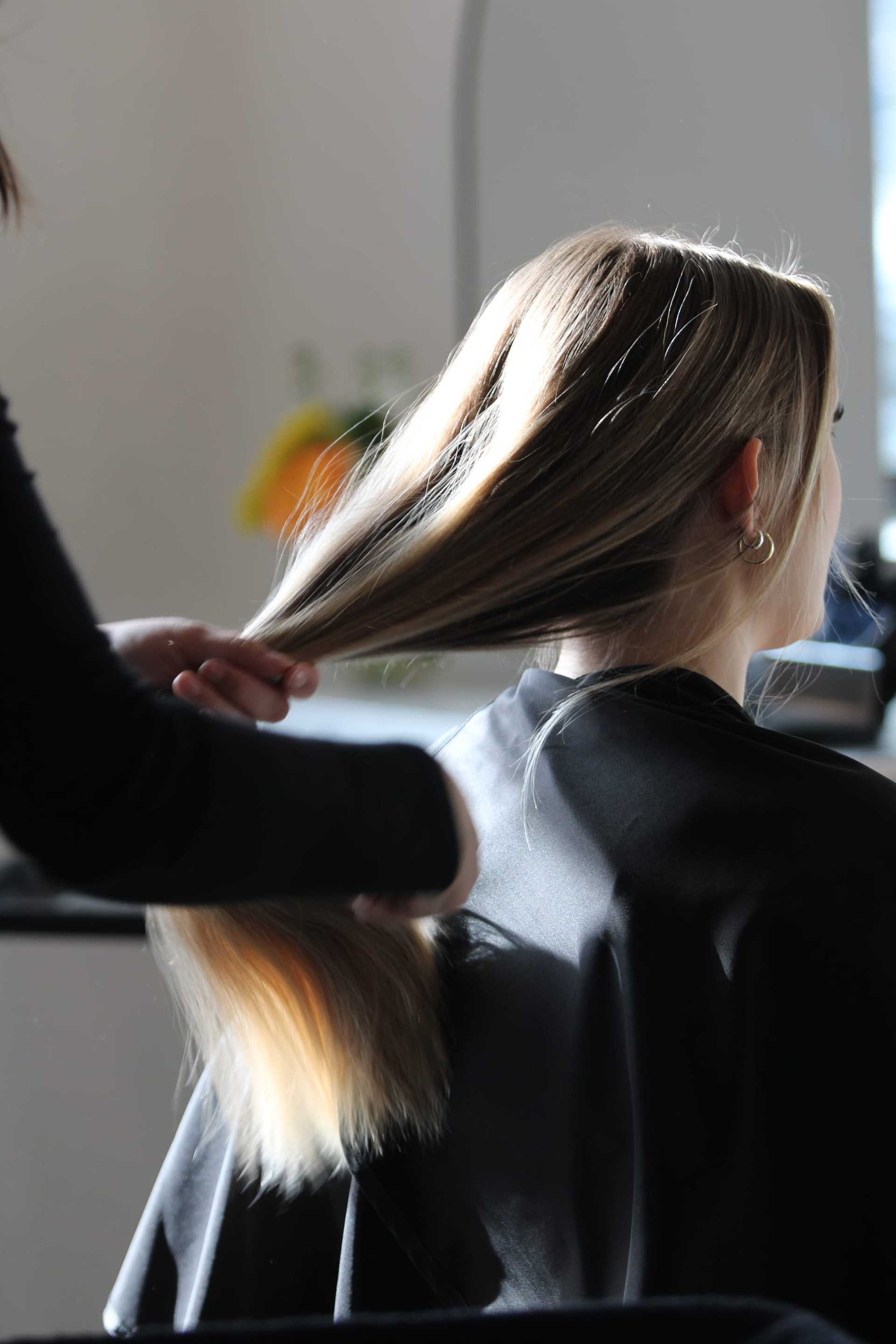 Hairdresser styling long, blonde hair in a salon setting.