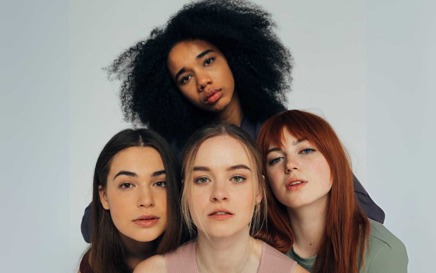 Four women with diverse hairstyles and expressions pose together for a portrait.