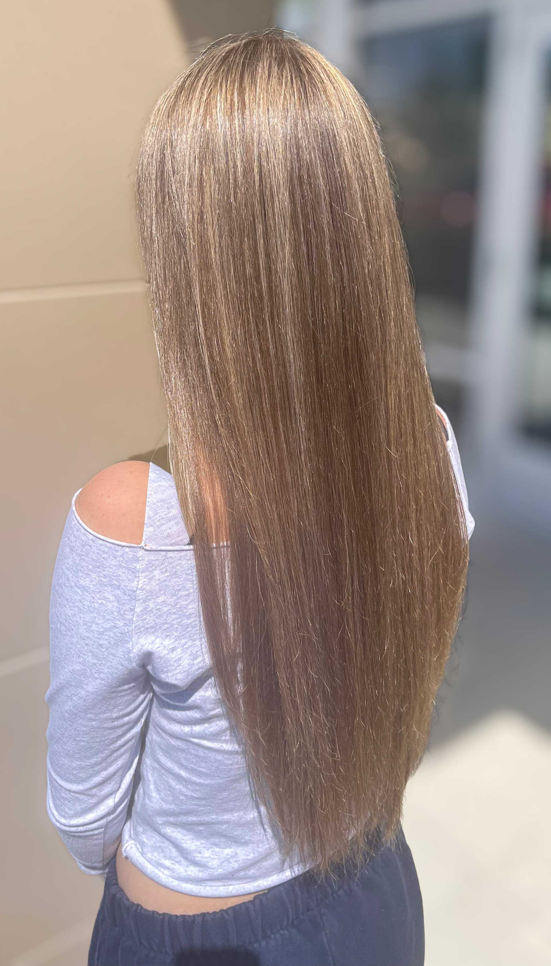 Long, straight, blonde hair on a person in a white top, viewed from the back.