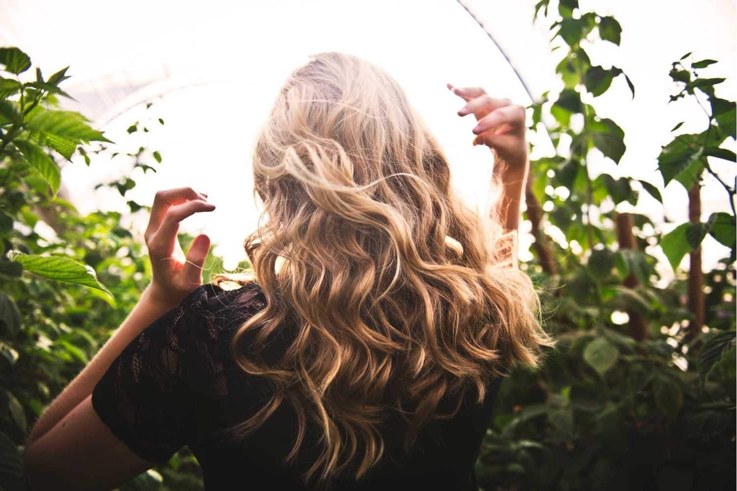 Woman with wavy blonde hair in a lush green garden.
