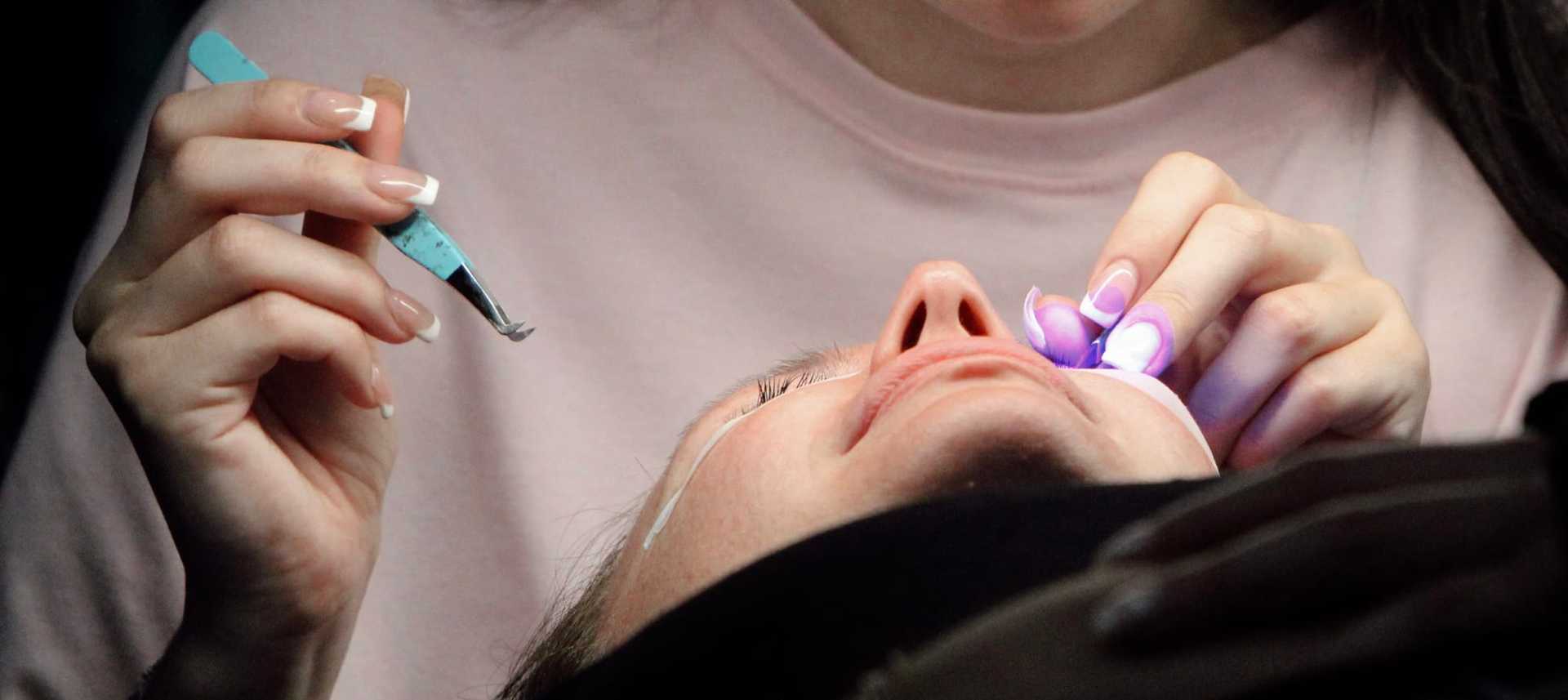 Applying eyelash extensions with precision tools and a small purple light.