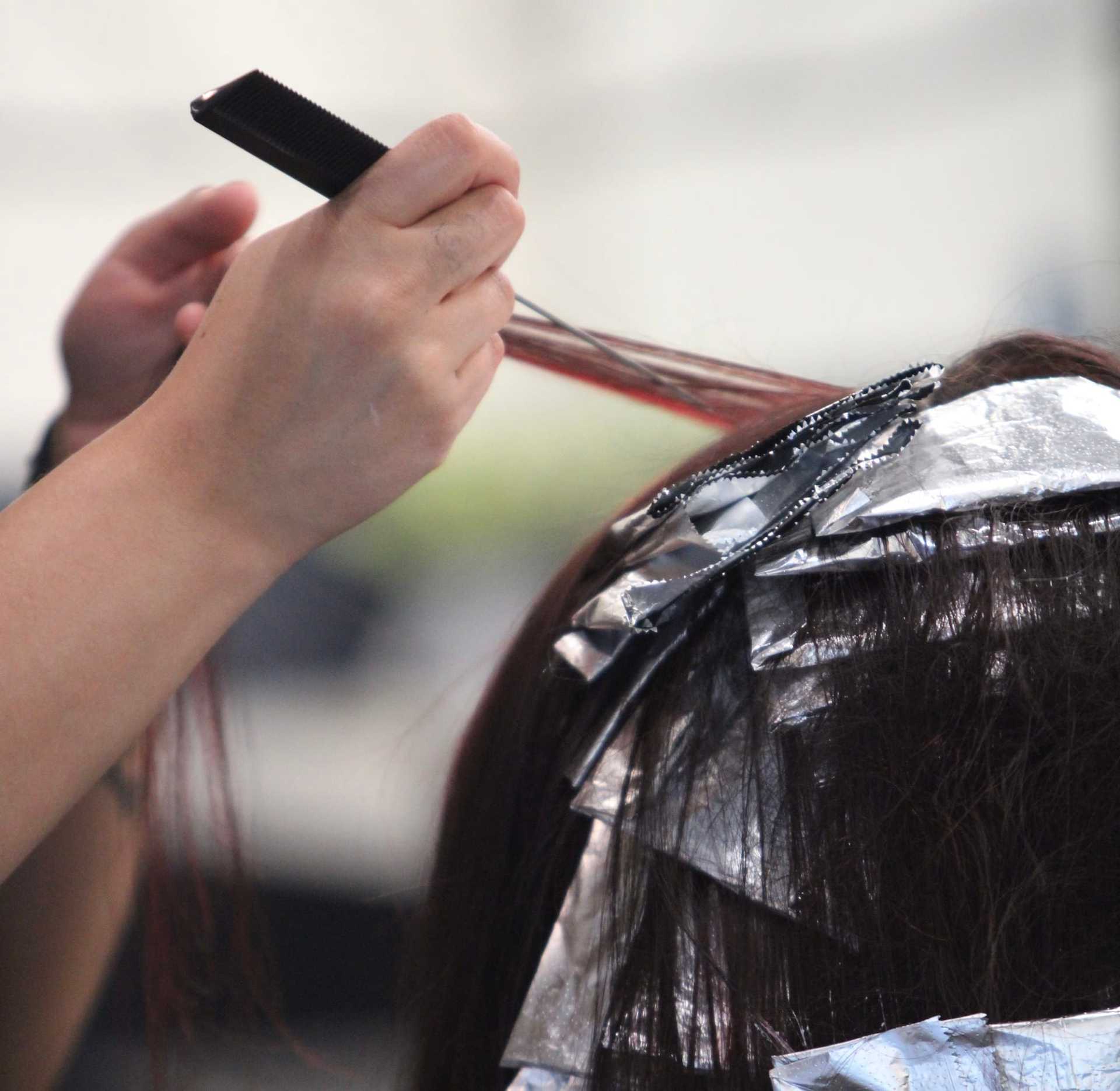 Hairdresser applying hair dye with foil and comb in a salon setting.